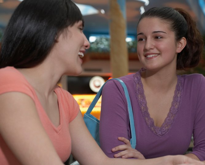 Two young women smiling and talking while sitting indoors